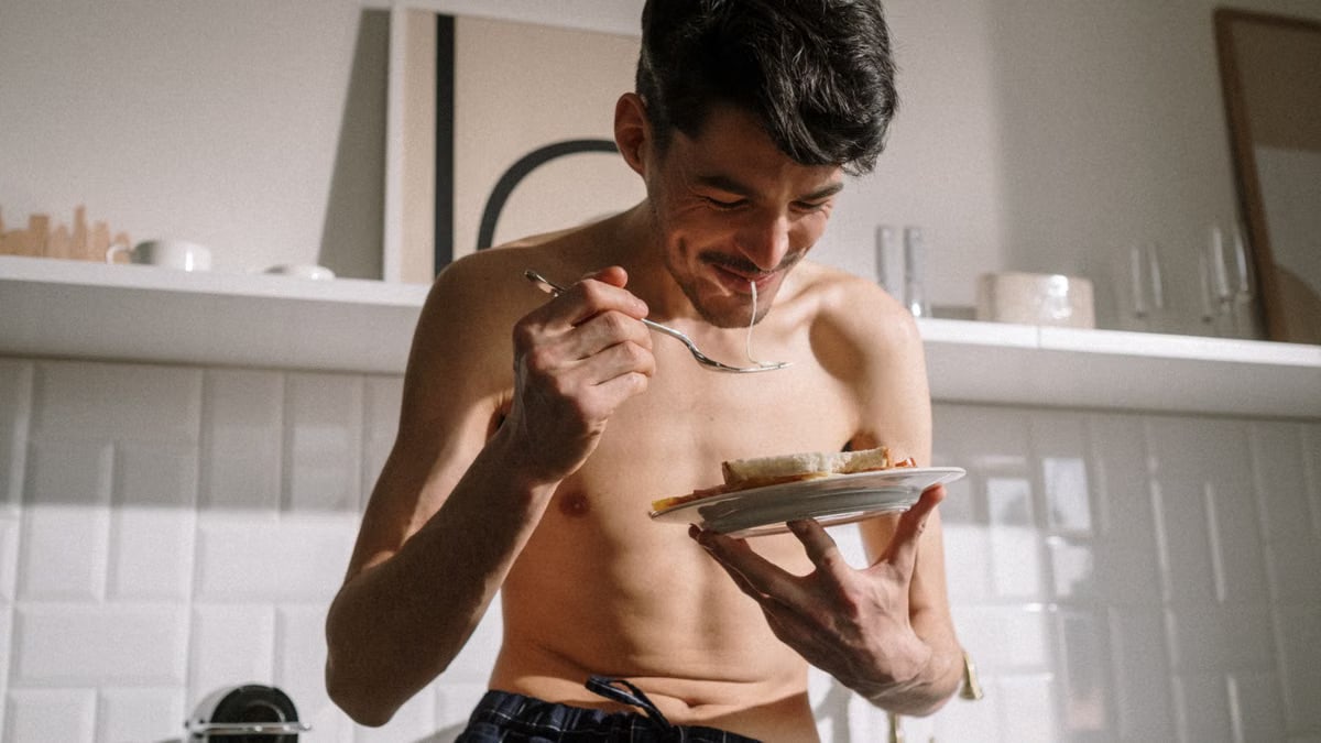 Smiling young man eats breakfast in a bright kitchen, enjoying a sunny morning.